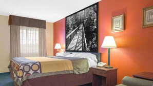 Une chambre d’hôtel avec un lit, deux lampes de chevet, une table de chevet avec un téléphone, une chaise et un grand tableau encadré au mur.
