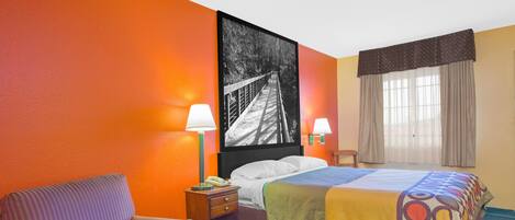 A hotel room with a bed, a chair, a nightstand, a lamp, and a window with curtains.