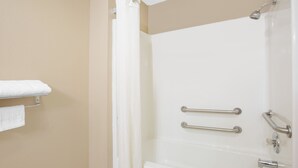 Une salle de bain avec une baignoire blanche, deux barres d’appui, une pomme de douche et un porte-serviettes avec une serviette blanche.