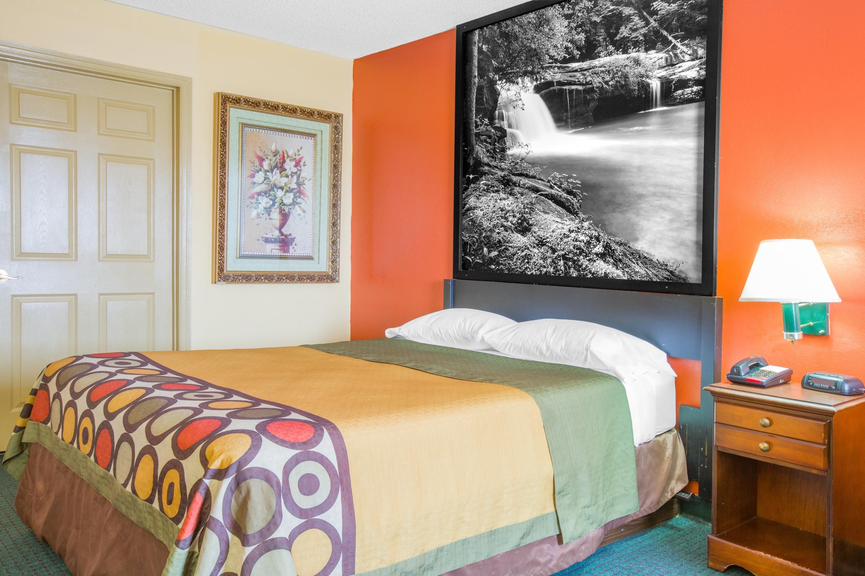 Habitación de hotel con cama, mesita de noche con lámpara, un cuadro enmarcado y una foto grande en la pared.