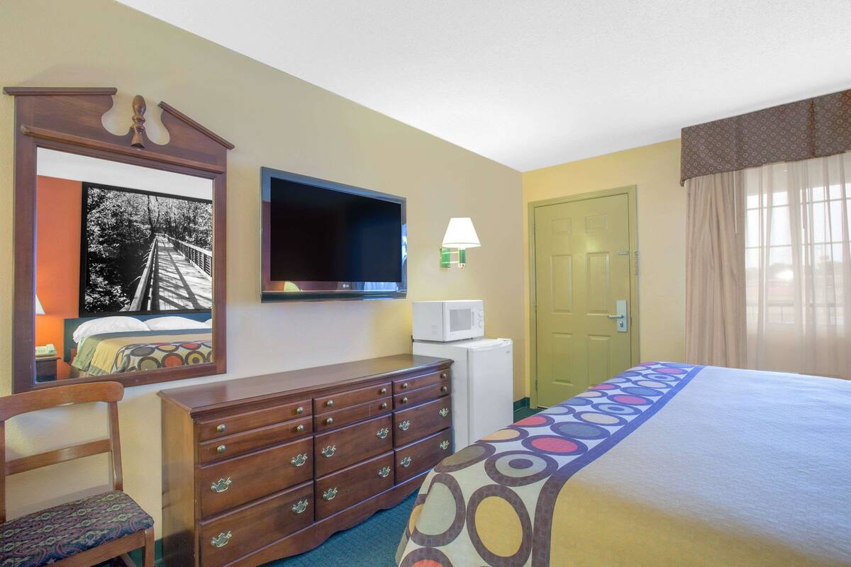 Habitación de hotel con cama, cómoda, televisor, microondas, puerta y ventana con cortinas.