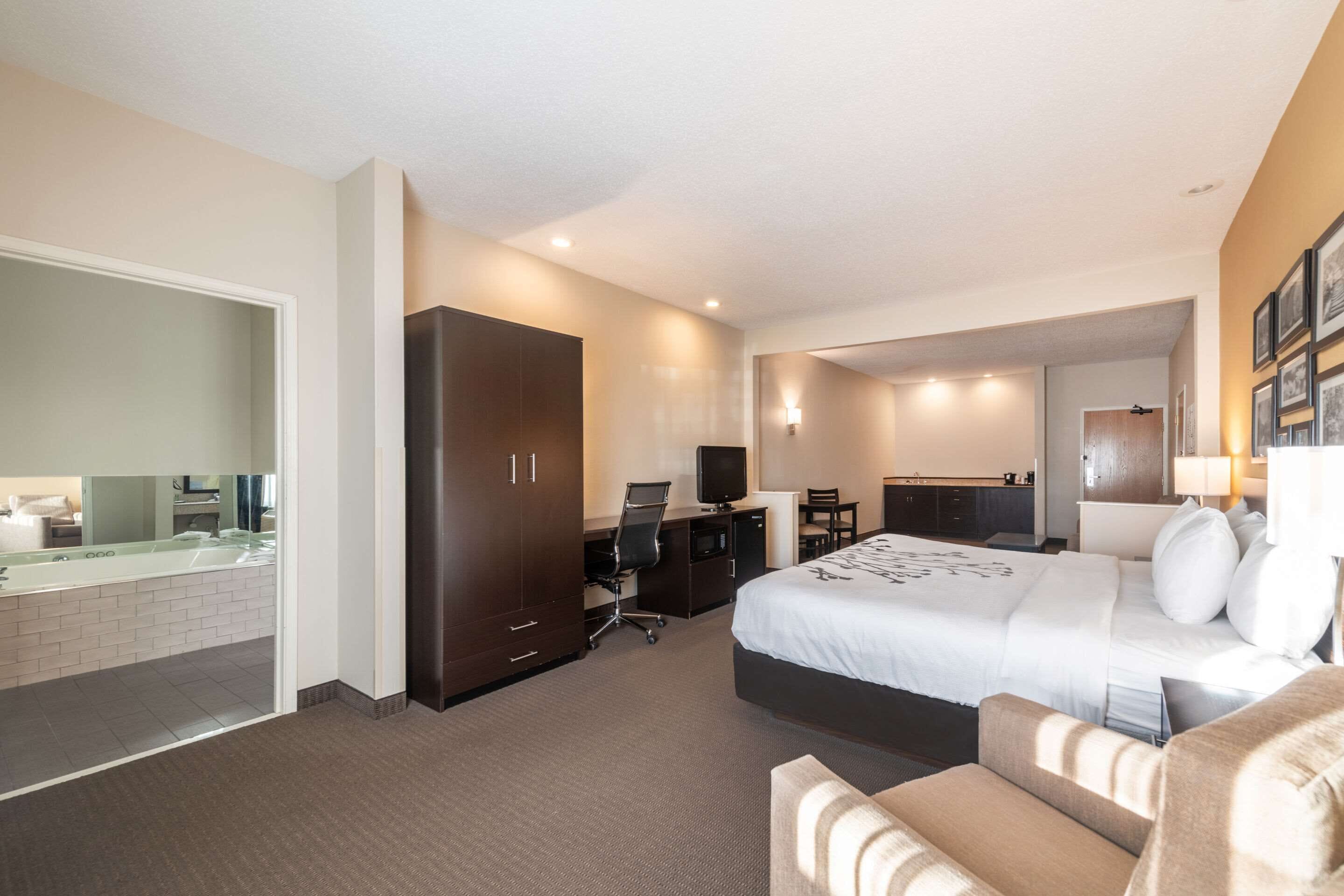 Hotelkamer met een groot bed, een bureau met computer, een televisie, een badkamer met spiegel en wastafel, en een zithoekje.