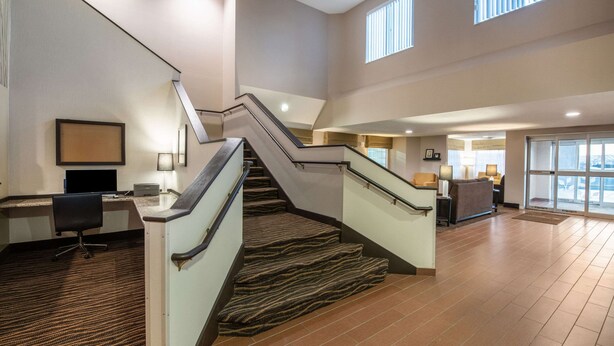 A spacious hotel lobby with a central staircase, a reception desk, and a seating area. - Sleep Inn & Suites Green Bay South (De Pere)