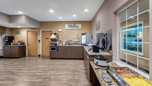 A hotel kitchen with a buffet setup, including a coffee station, a refrigerator, and a food display. - Sleep Inn & Suites Green Bay South (De Pere)