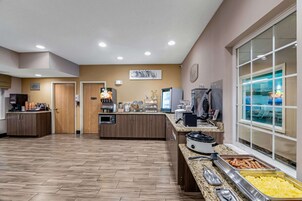 A hotel kitchen with a buffet setup, including a coffee station, a refrigerator, and a food display.