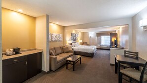 A hotel room with a kitchenette, a sofa, a bed, a dining table, and a TV. - Sleep Inn & Suites Green Bay South (De Pere)