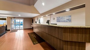 A reception area with a wooden reception desk, a clock, and a framed artwork on the wall. - Sleep Inn & Suites Green Bay South (De Pere)