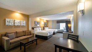A hotel room with a sofa, two single beds, a dining table, and a TV. - Sleep Inn & Suites Green Bay South (De Pere)