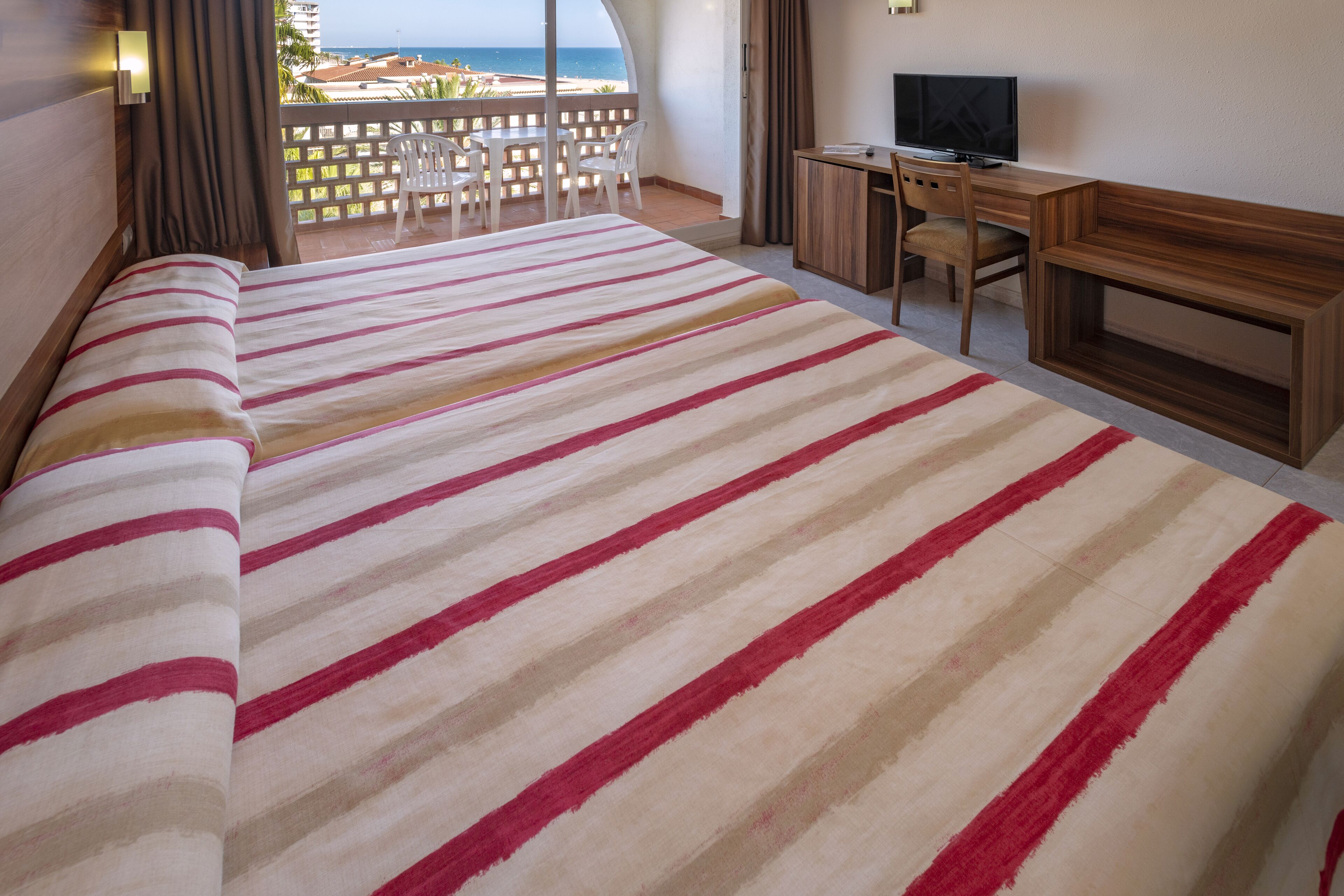 Une chambre d’hôtel avec un grand lit, un bureau avec une télévision et un balcon donnant sur la plage.
