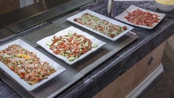 Un bufé con diversos platos, entre ellos ensaladas, carnes y guarniciones.