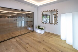 Un interior moderno con un separador de vidrio, una maceta blanca con flores y un espejo grande con un marco ornamentado.
