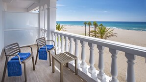 A balcony with two chairs and a table, overlooking a beach with palm trees and the ocean. - 4R Gran Europe (El Vendrell)