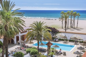 Un área de piscina con sillas de descanso, una alberca y vistas a la playa y al océano.