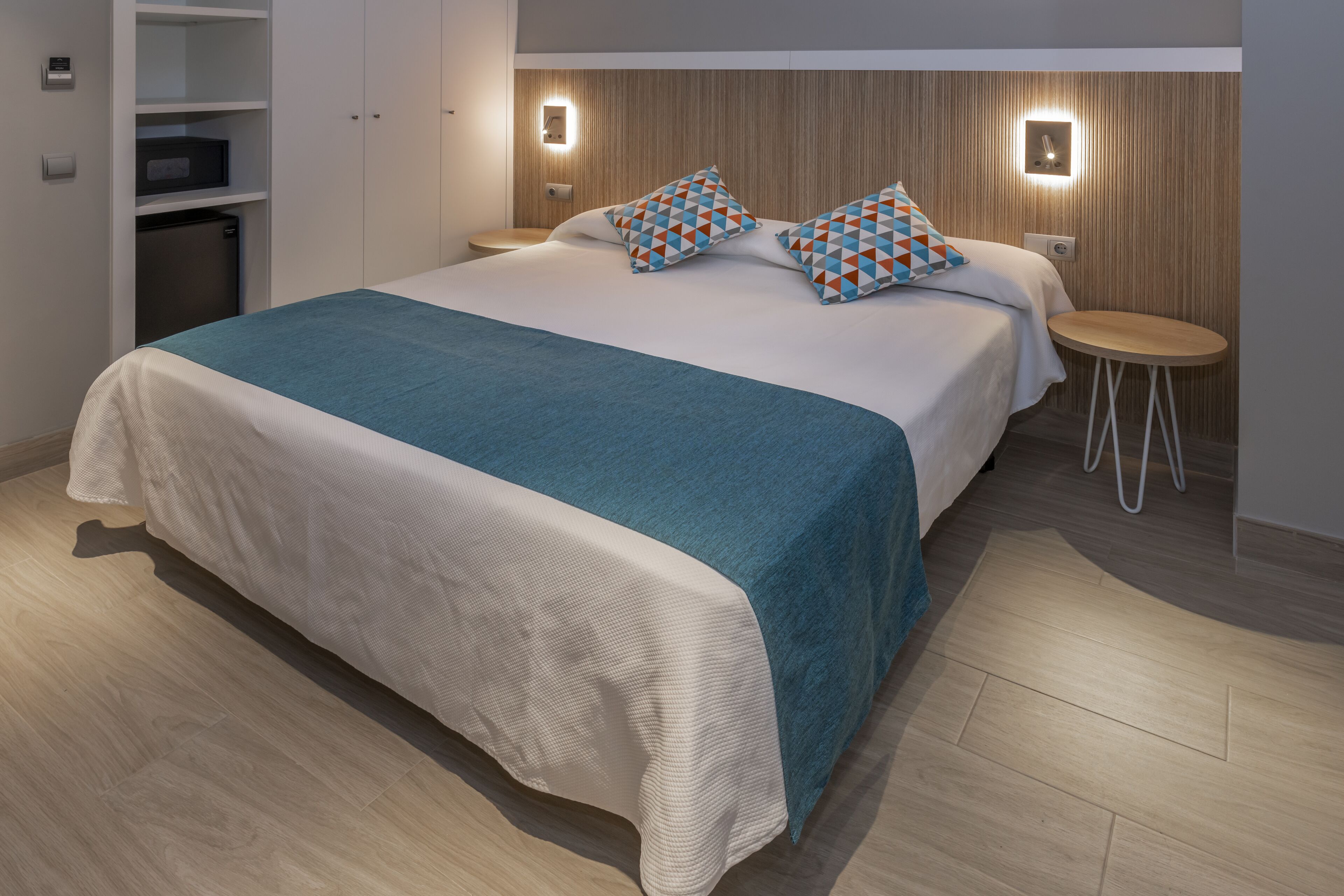 A modern hotel room with a large bed, a small desk, and built-in storage.