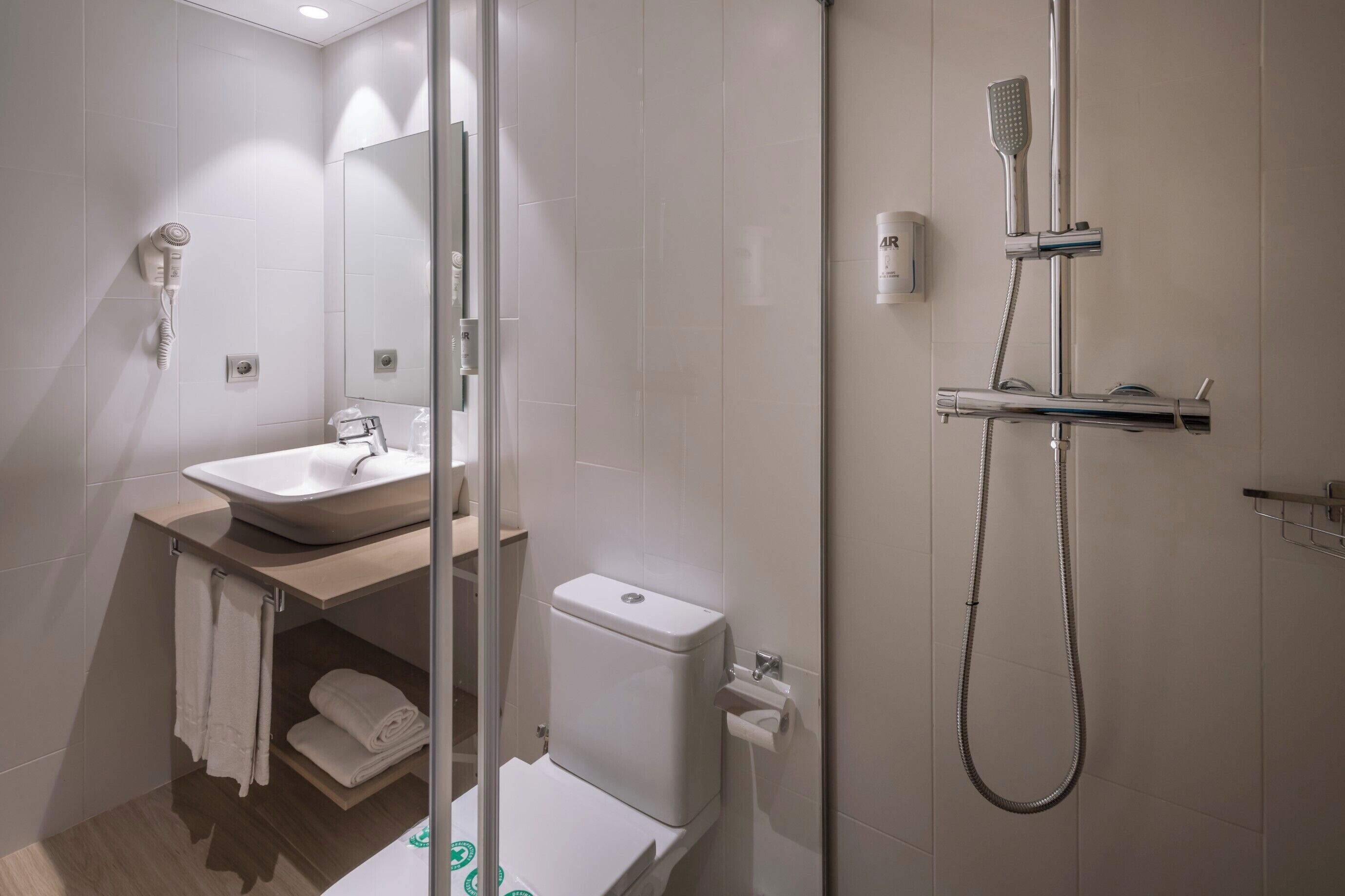 Un baño moderno con ducha de vidrio, lavabo con espejo y retrete.