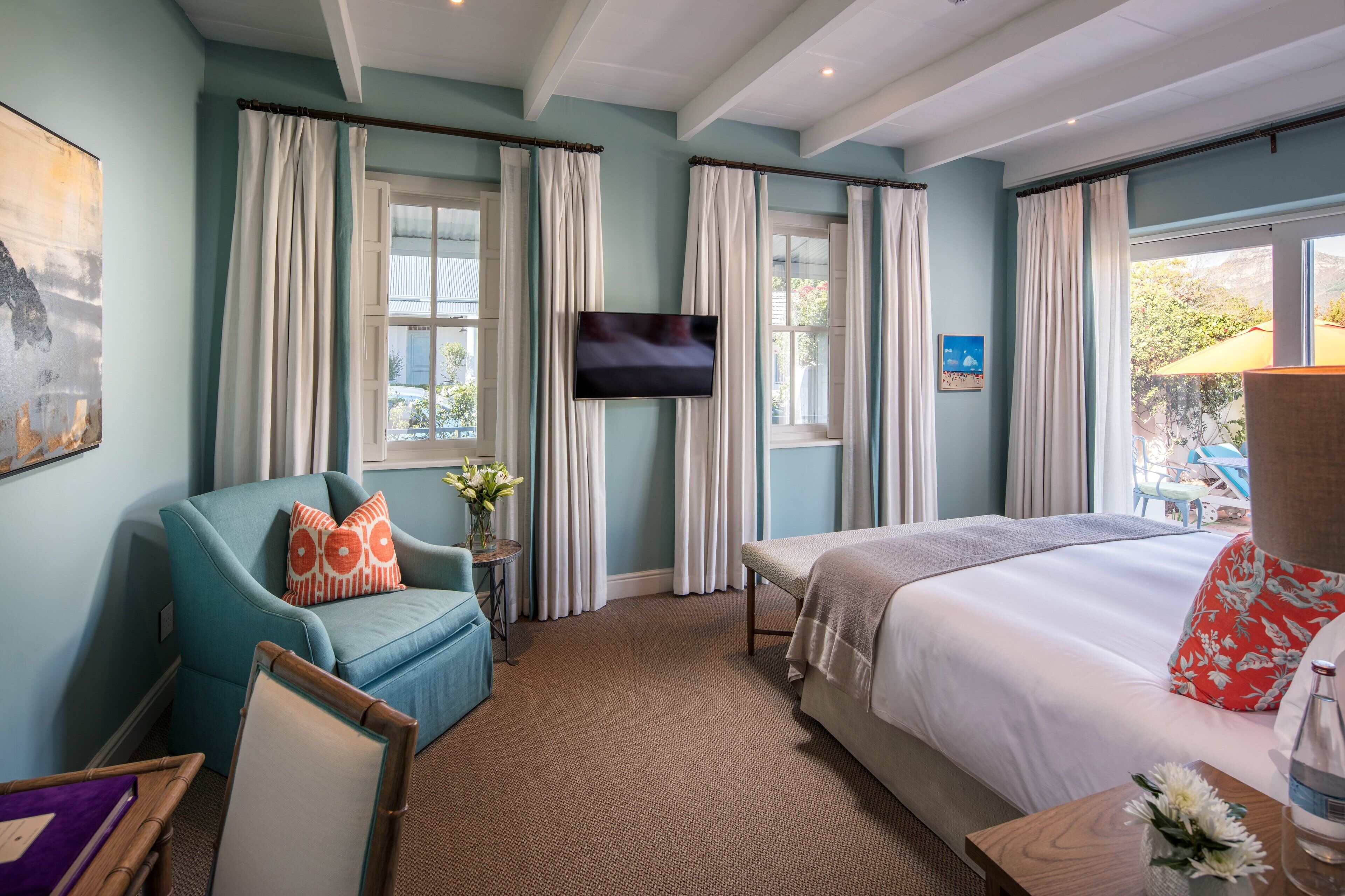 Ein Hotelzimmer mit einem Bett, einem Fernseher, einem Sessel und einem Fenster mit Vorhängen.