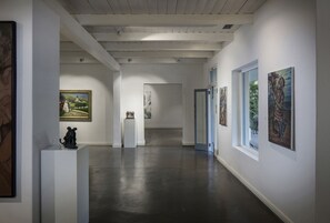 A gallery with artworks on display, a polished floor, and a wooden ceiling.