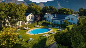 Ein großes Haus mit Swimmingpool, umgeben von üppiger Vegetation und Bergen im Hintergrund.