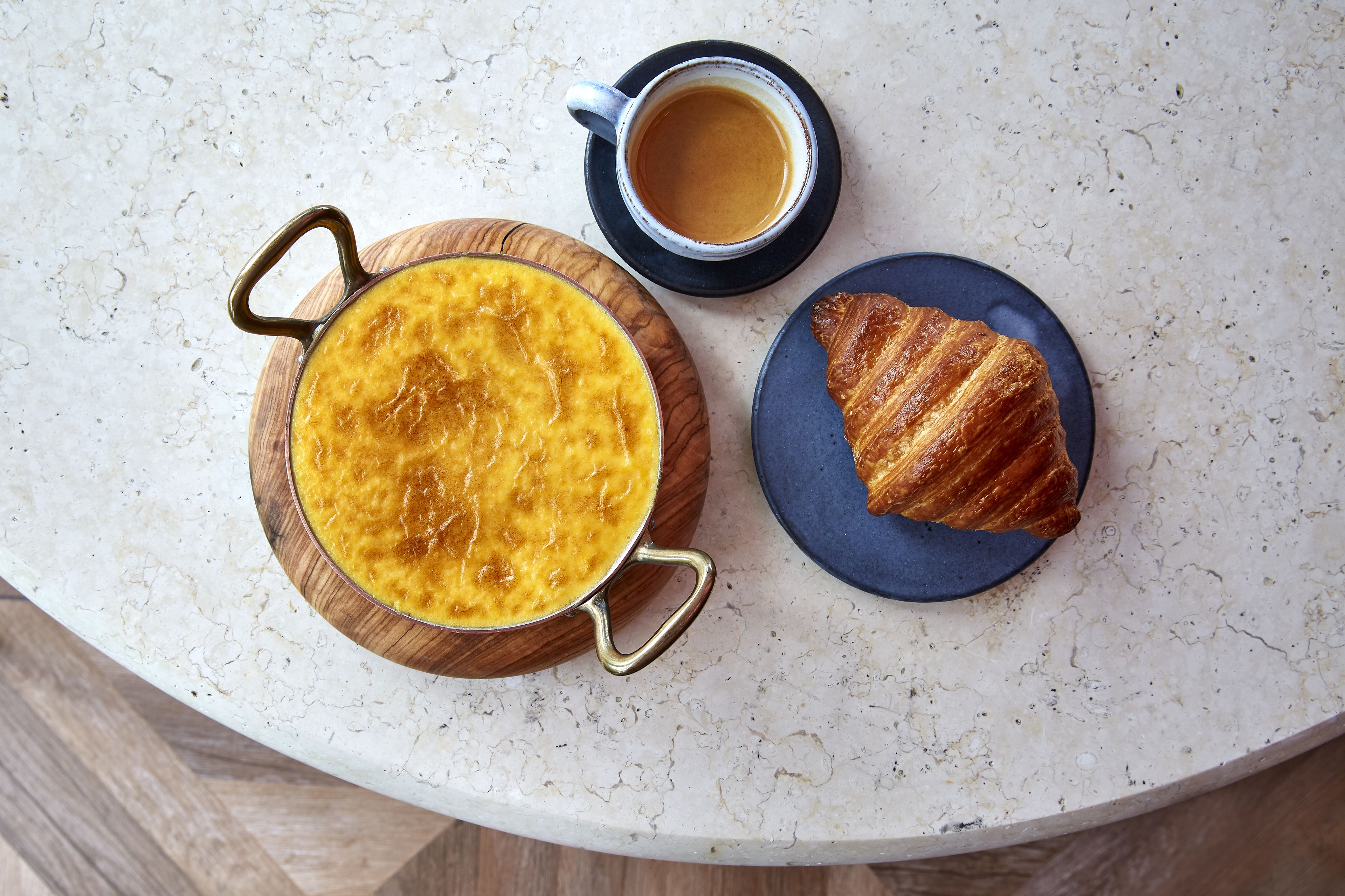 Ein Frühstückstisch mit einer Puddingkanne, einer Kaffeetasse und einem Croissant auf einer Marmortafel.