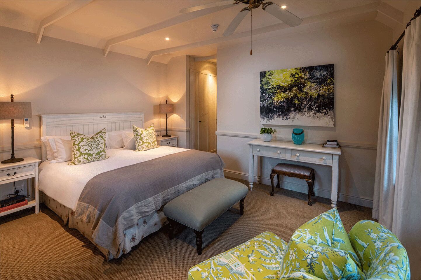 A bedroom with a large bed, bedside tables, a desk, and a chair.