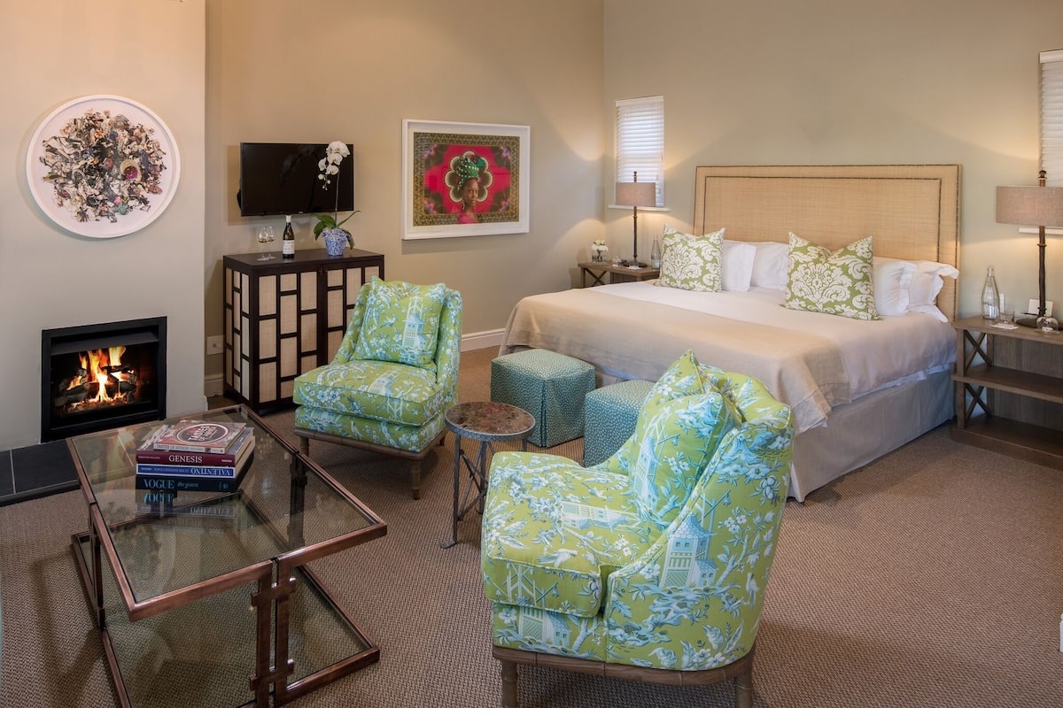 Une chambre d’hôtel comprenant un lit, deux fauteuils, une petite table, une cheminée et un téléviseur.