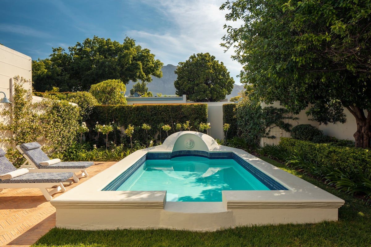 Une piscine entourée de chaises longues, de verdure et d’arbres.