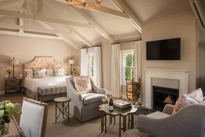 A spacious bedroom with a large bed, a sitting area with a fireplace, and a television mounted on the wall.