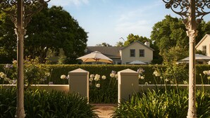 Ein Gartenweg mit einer Pergola, einer Hecke und einem Gebäude im Hintergrund.