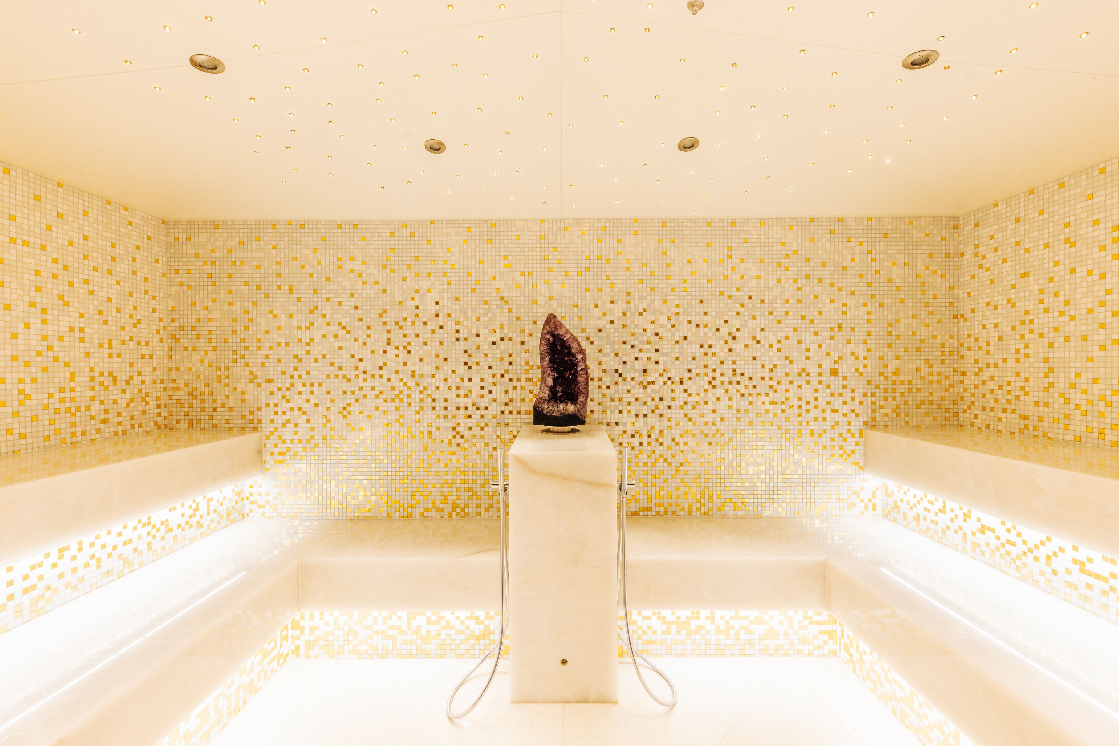 Un baño con paredes de mosaicos, una columna central y una bañera.