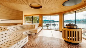 Un interior moderno con techo de madera, una zona de estar con asientos curvados y un amplio ventanal con vistas a un lago.