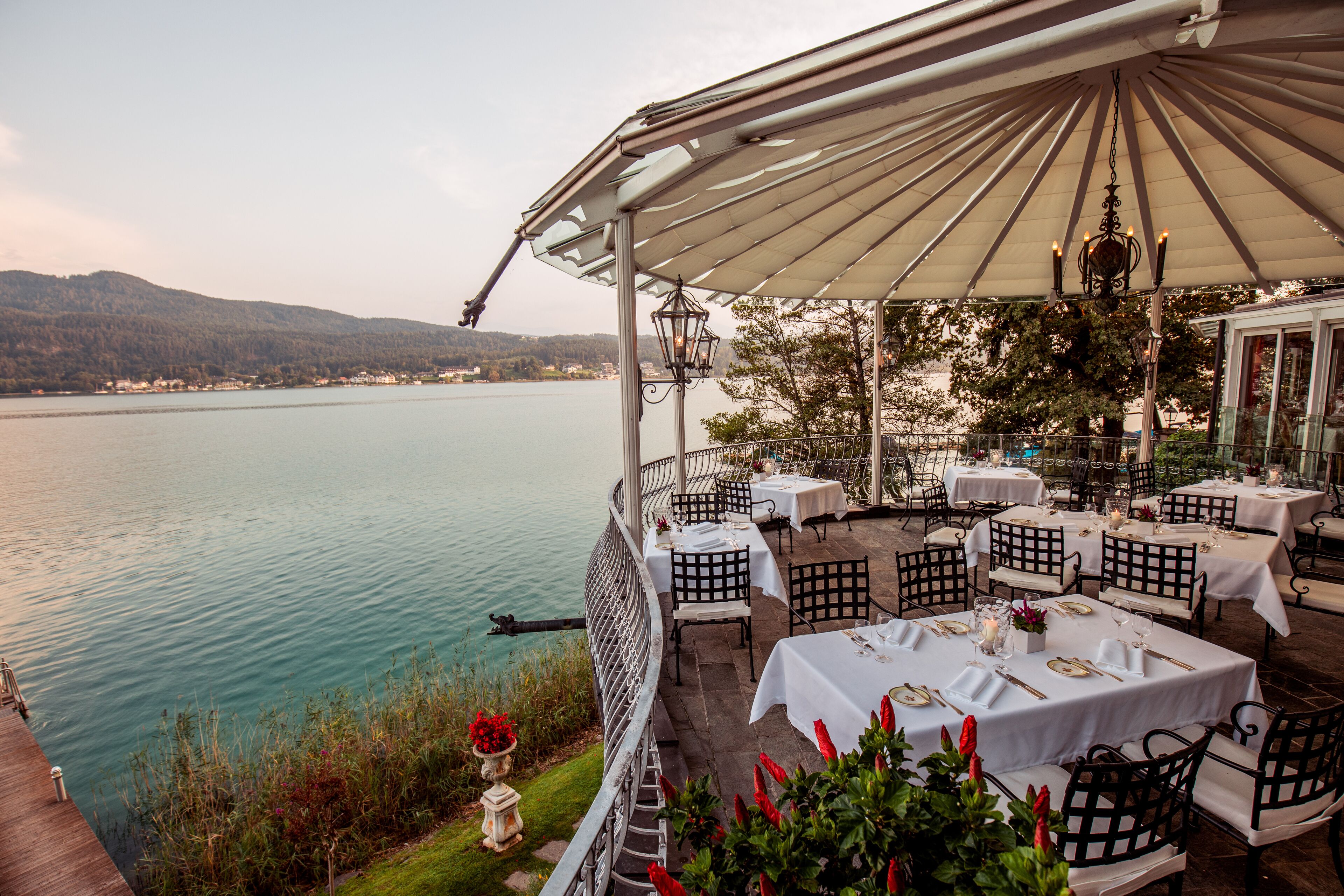 A lakeside restaurant with outdoor seating, tables set for dining, and a view of the lake.