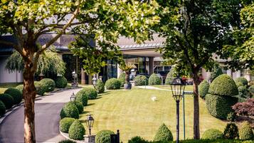 A well-maintained garden with neatly trimmed hedges, a curved driveway, and a building with large windows in the background.