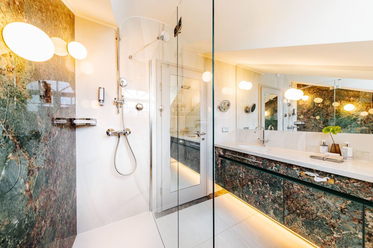 Un baño moderno con cabina de ducha de vidrio, encimera de mármol y un espejo grande.