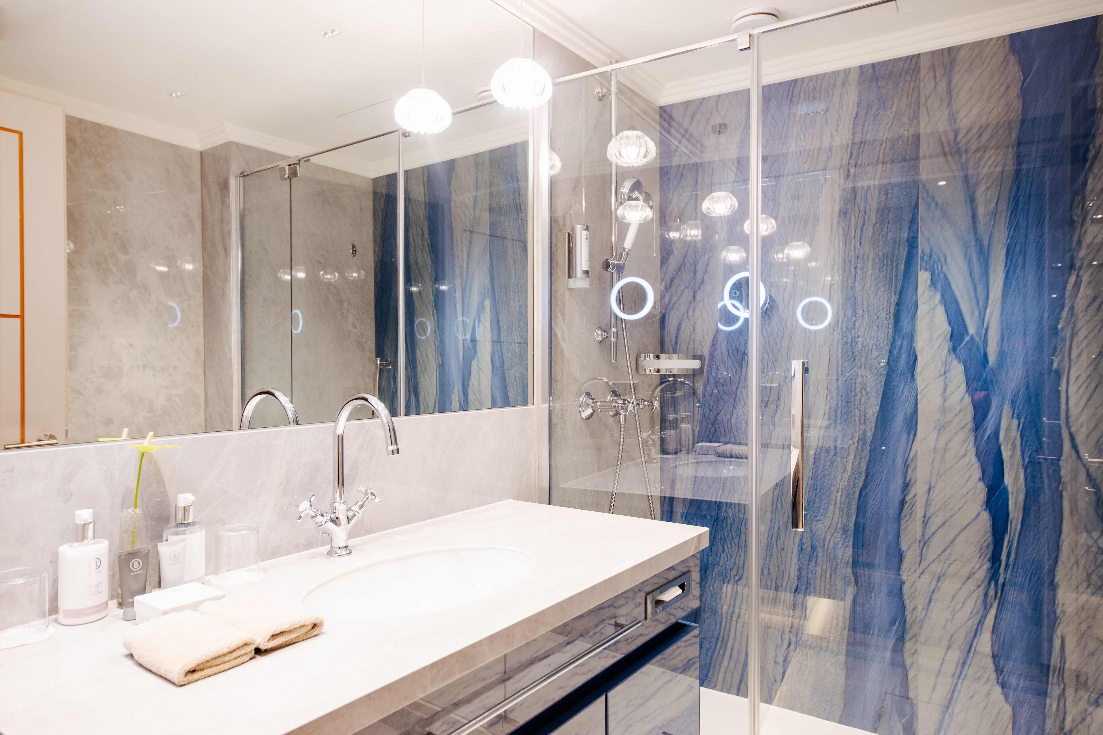 A modern bathroom with a glass-enclosed shower, a large mirror, and a white sink with a marble countertop.