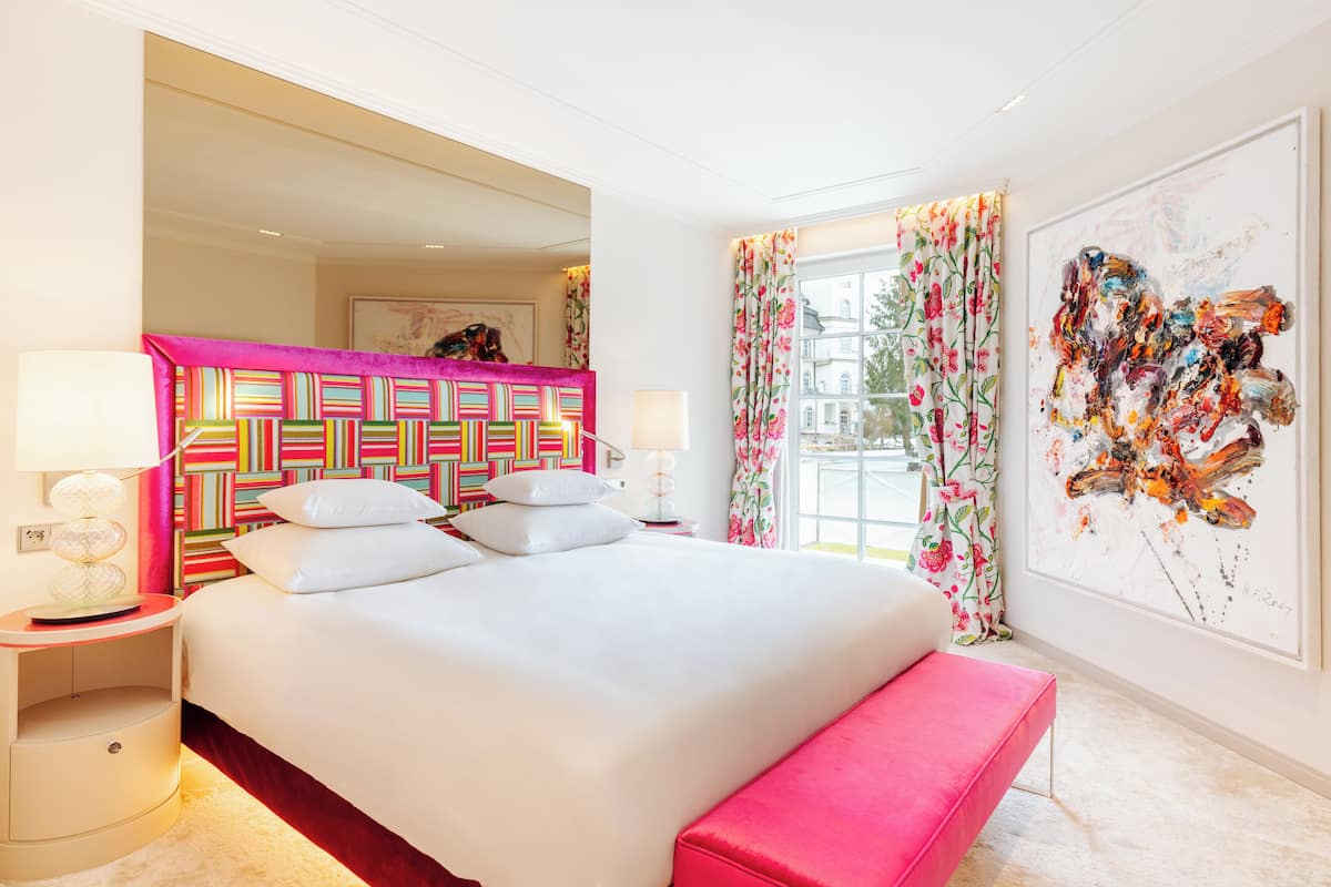 Una habitación de hotel moderna con una cama grande, un banco rosa y un cabecero colorido.