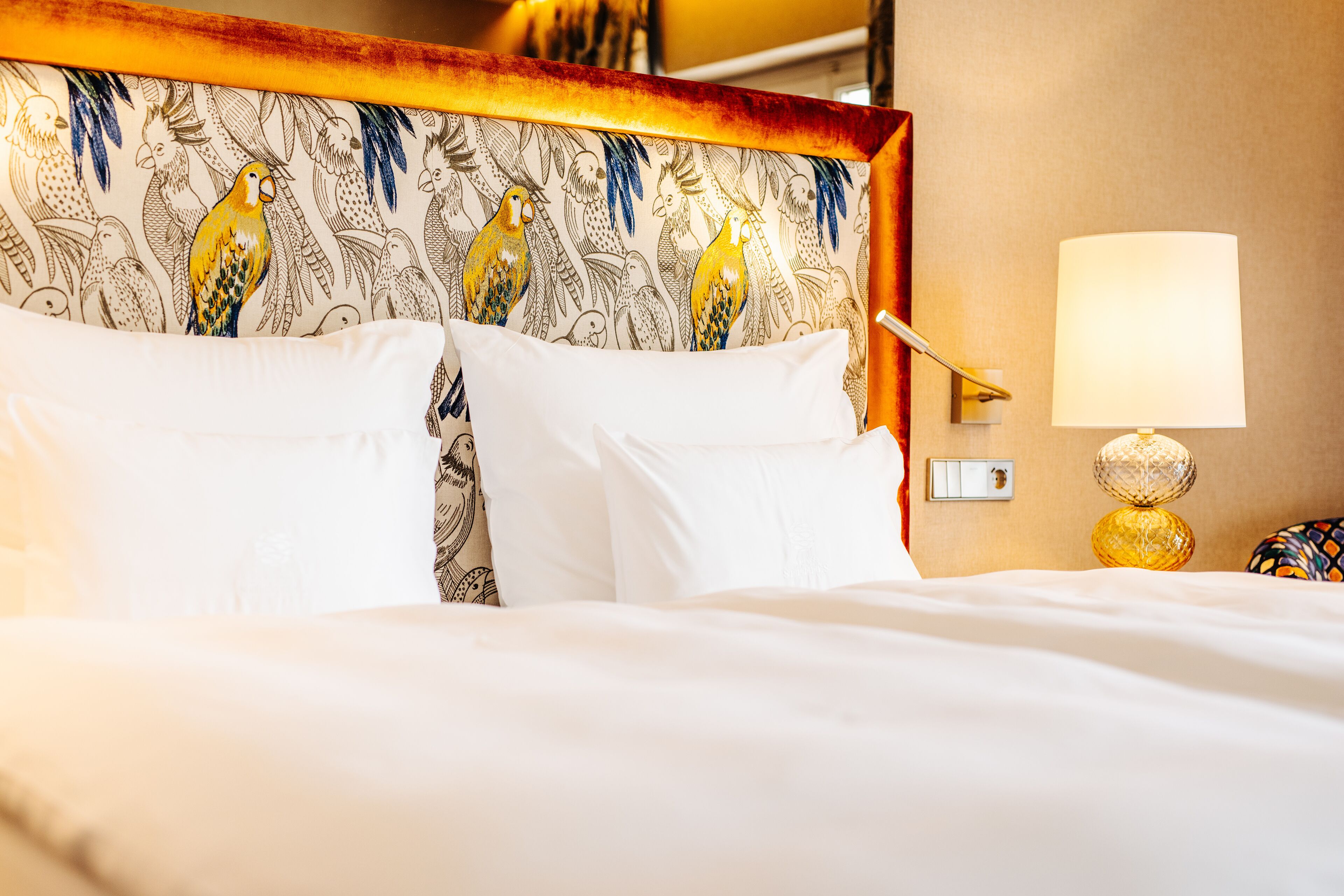 A neatly made bed with white linens, a patterned headboard, and a bedside lamp.