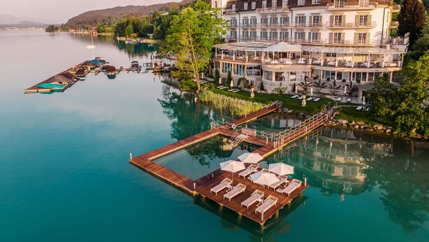 Un gran hotel de varios pisos con vistas al agua, un muelle con sillones de descanso y una zona de piscina.