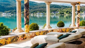 Una terraza con tumbonas, un muro de mosaico y vistas a un lago y montañas.