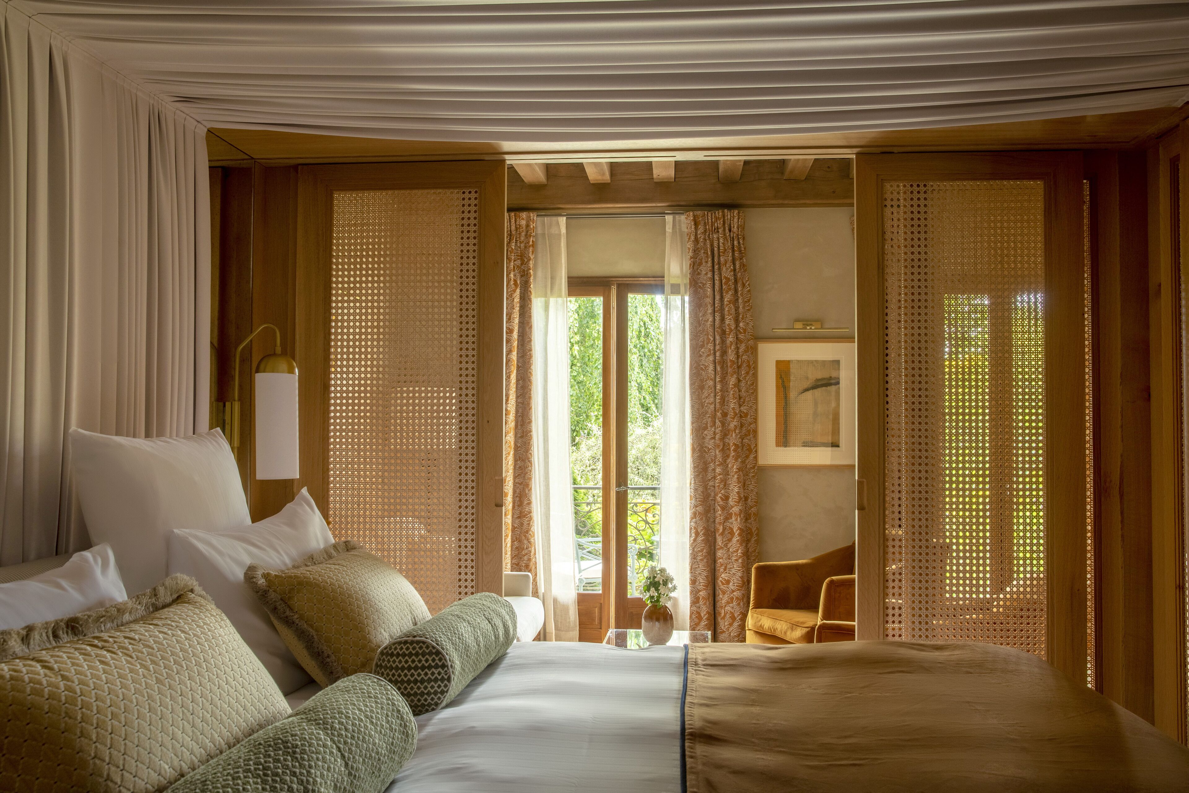 Quarto de hotel com uma cama grande, uma mesa pequena, uma cadeira e uma janela com cortinas.
