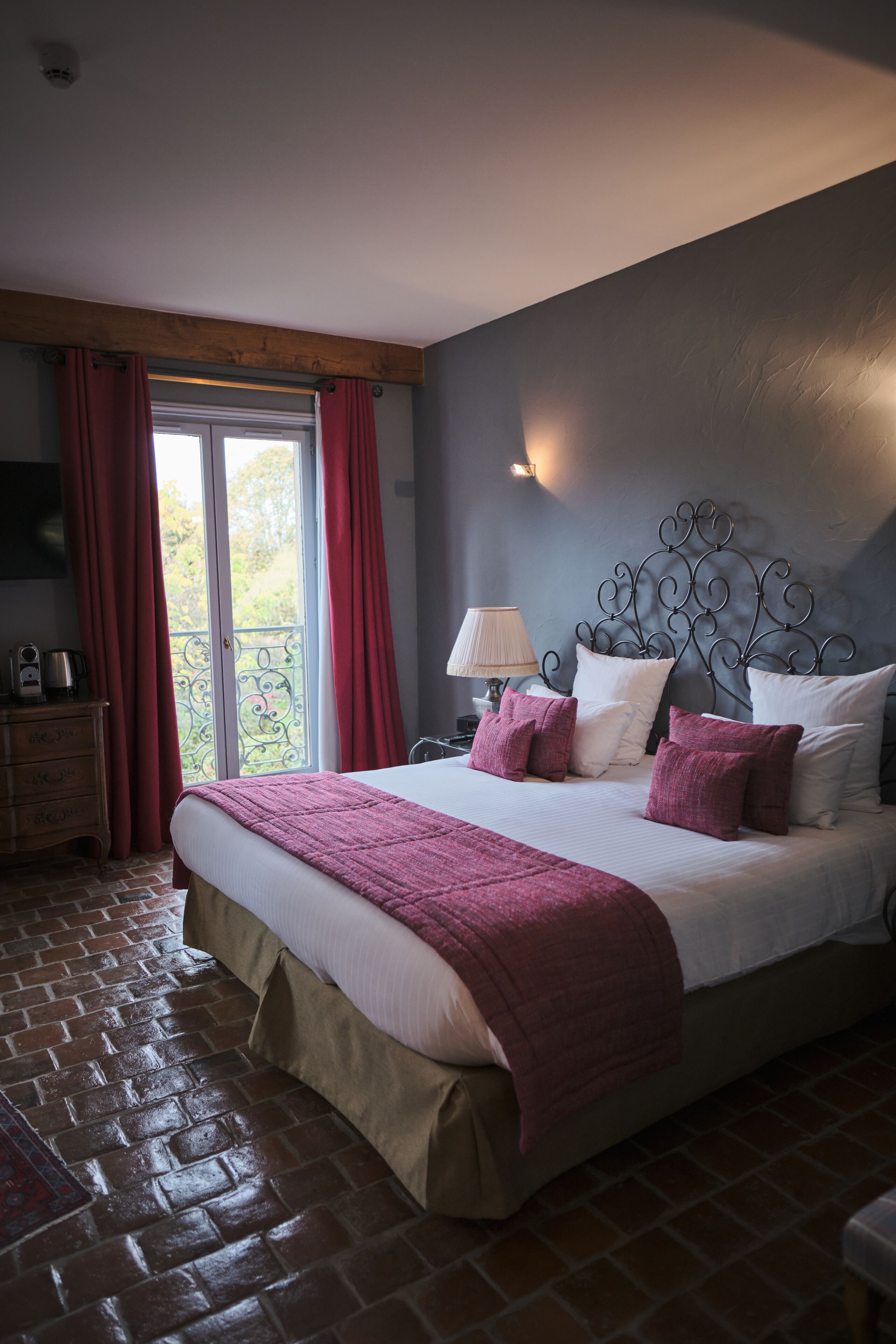 A bedroom with a large bed, a wooden headboard, a nightstand with a lamp, and a view of the outdoors through a sliding glass door.