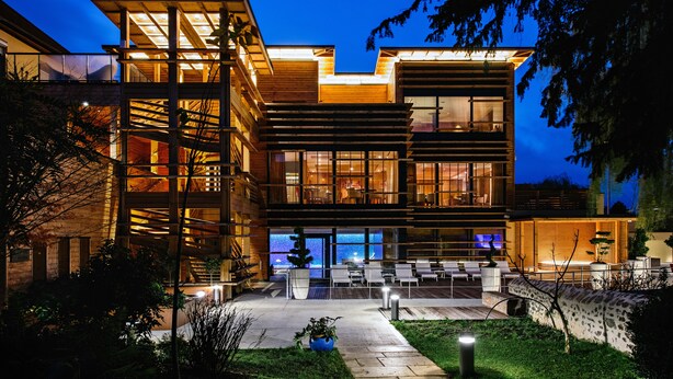Un edificio moderno de varios pisos con una entrada bien iluminada, un área de estar al aire libre y una escalera visible que conduce a los niveles superiores.