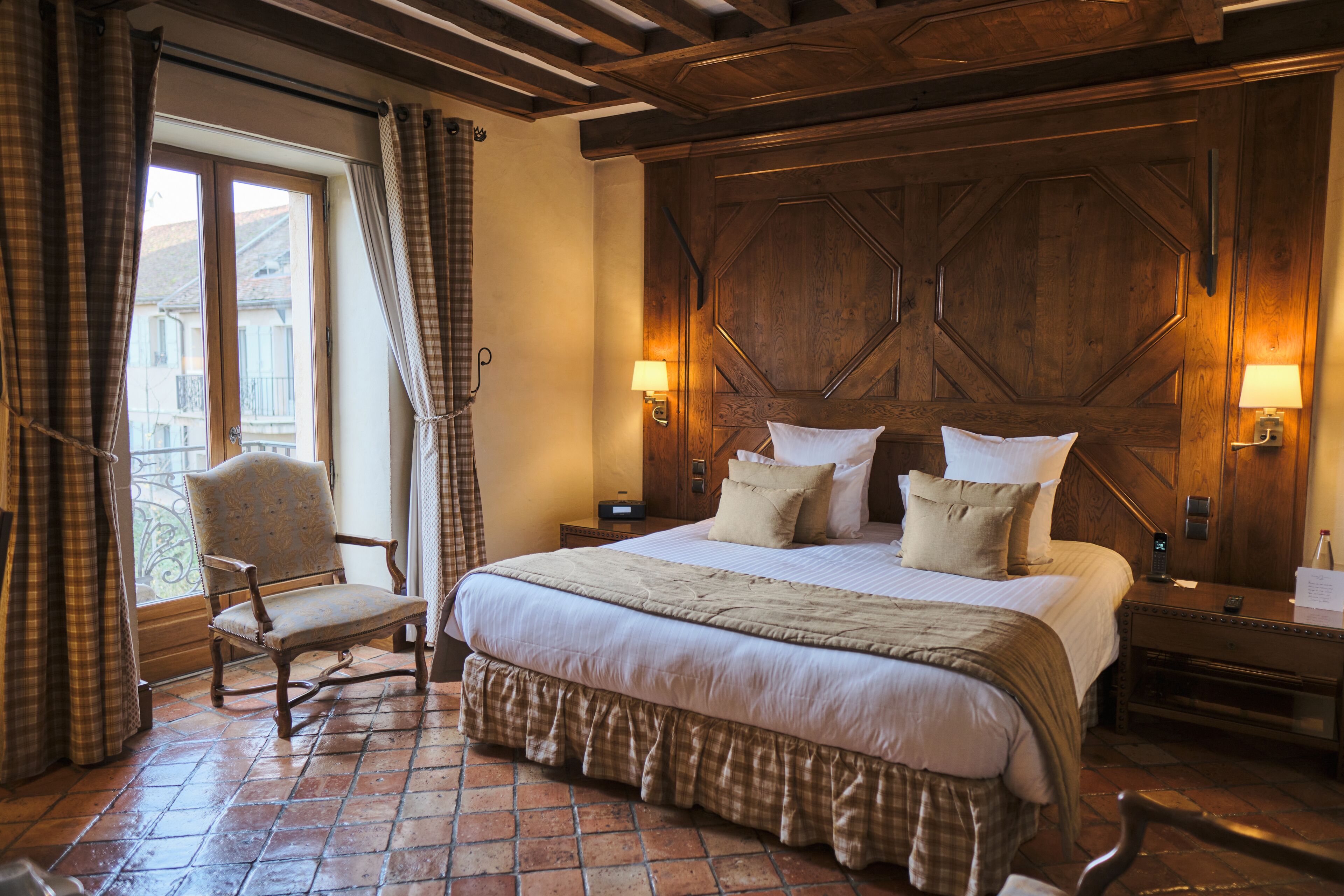 Habitación de hotel con una cama grande, una silla, cabecera de madera y ventana con cortinas.