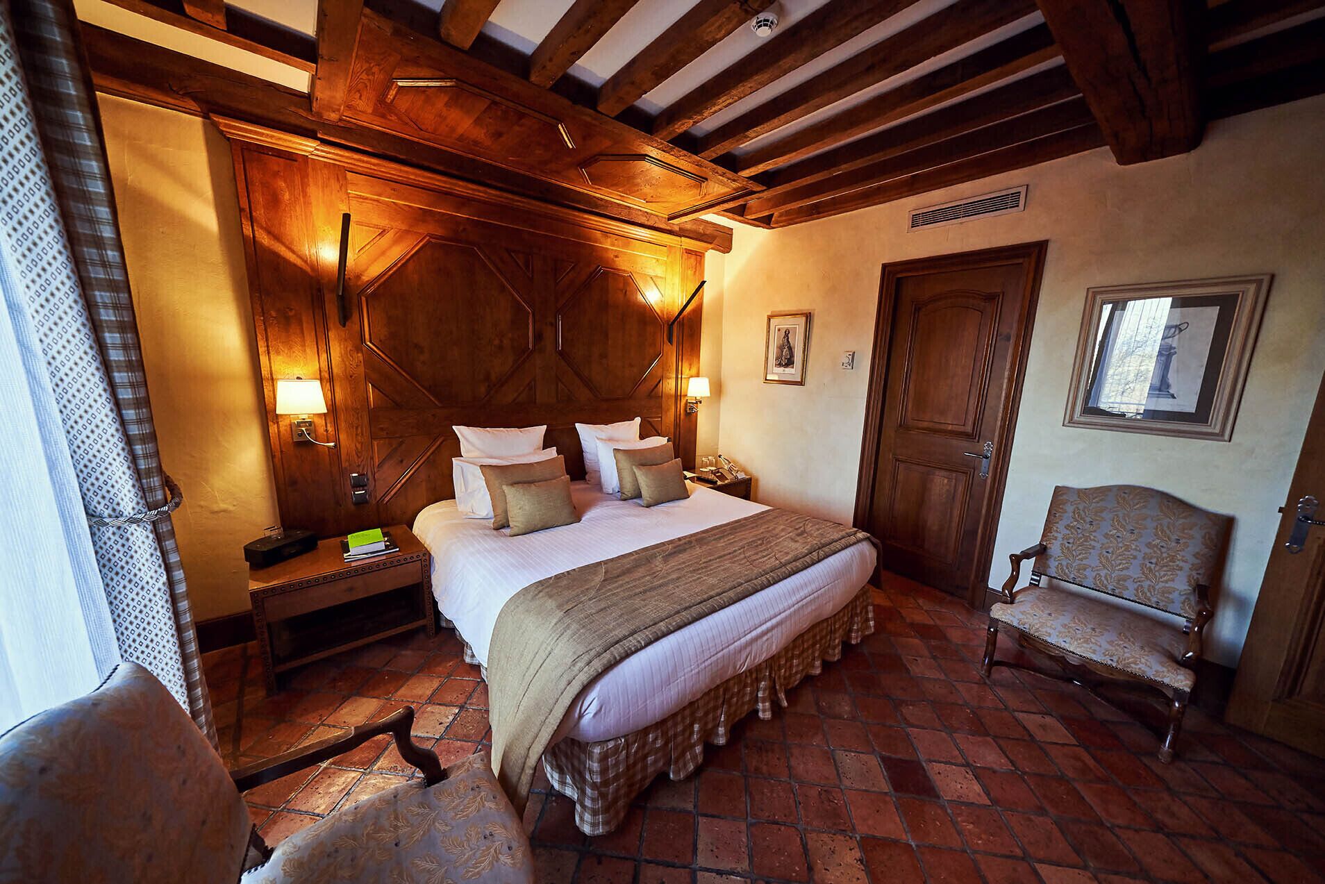 A traditional room with a large bed, wooden headboard, and a classic chair.