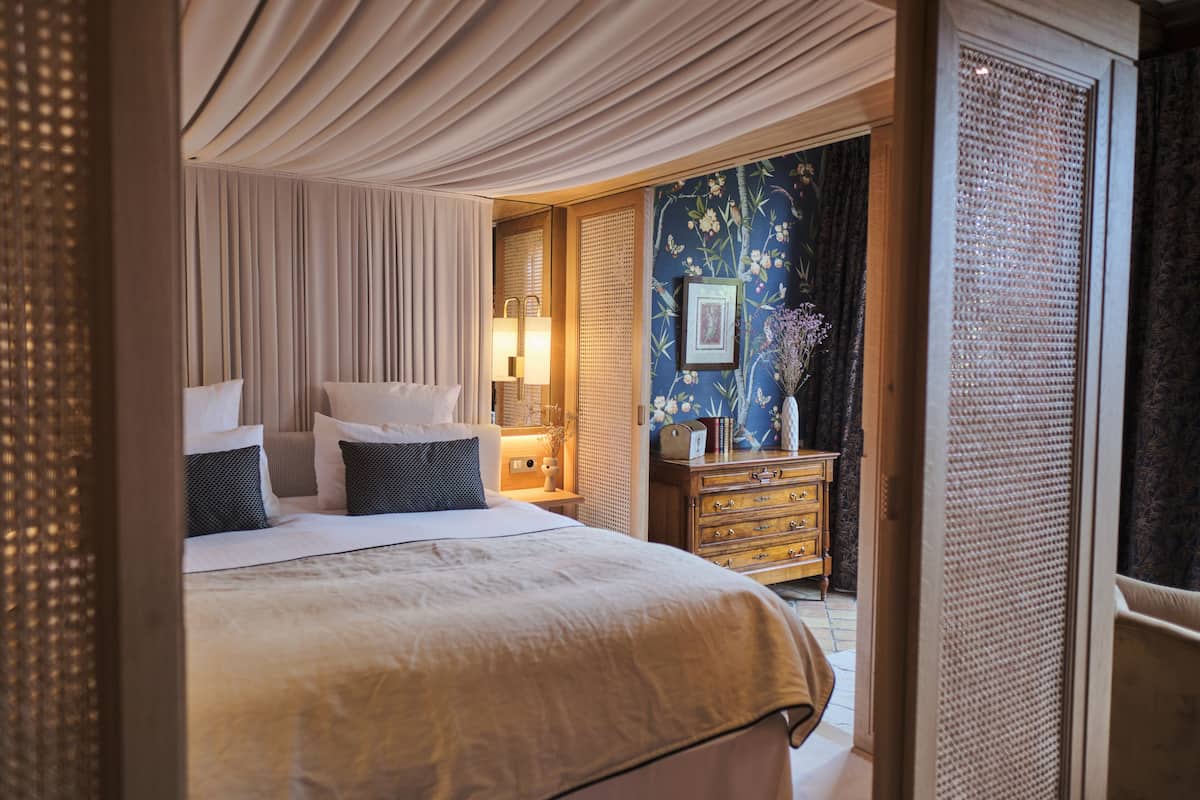 Habitación de hotel con una cama grande, una mesita de noche con lámpara, un aparador y un jarrón decorativo.