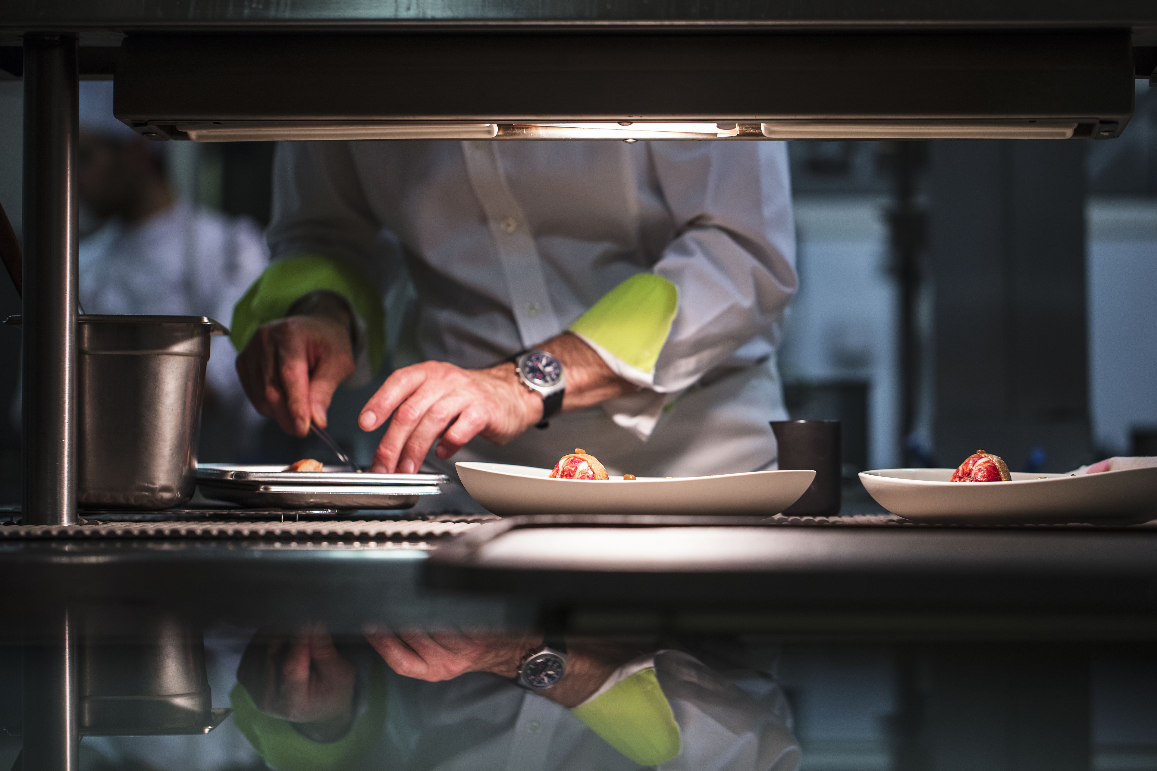 Un chef preparando comida debajo de una campana extractora, con una superficie reflectante abajo.