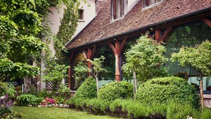 Un edificio tradicional con techo inclinado, vigas de madera y un jardín cuidado con diversas plantas y flores.