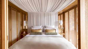 Habitación de hotel con una cama grande, cabecero de madera y techo con tela drapeada.