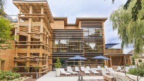 Un edificio moderno con fachada de madera, ventanas amplias y terraza exterior con sombrillas.