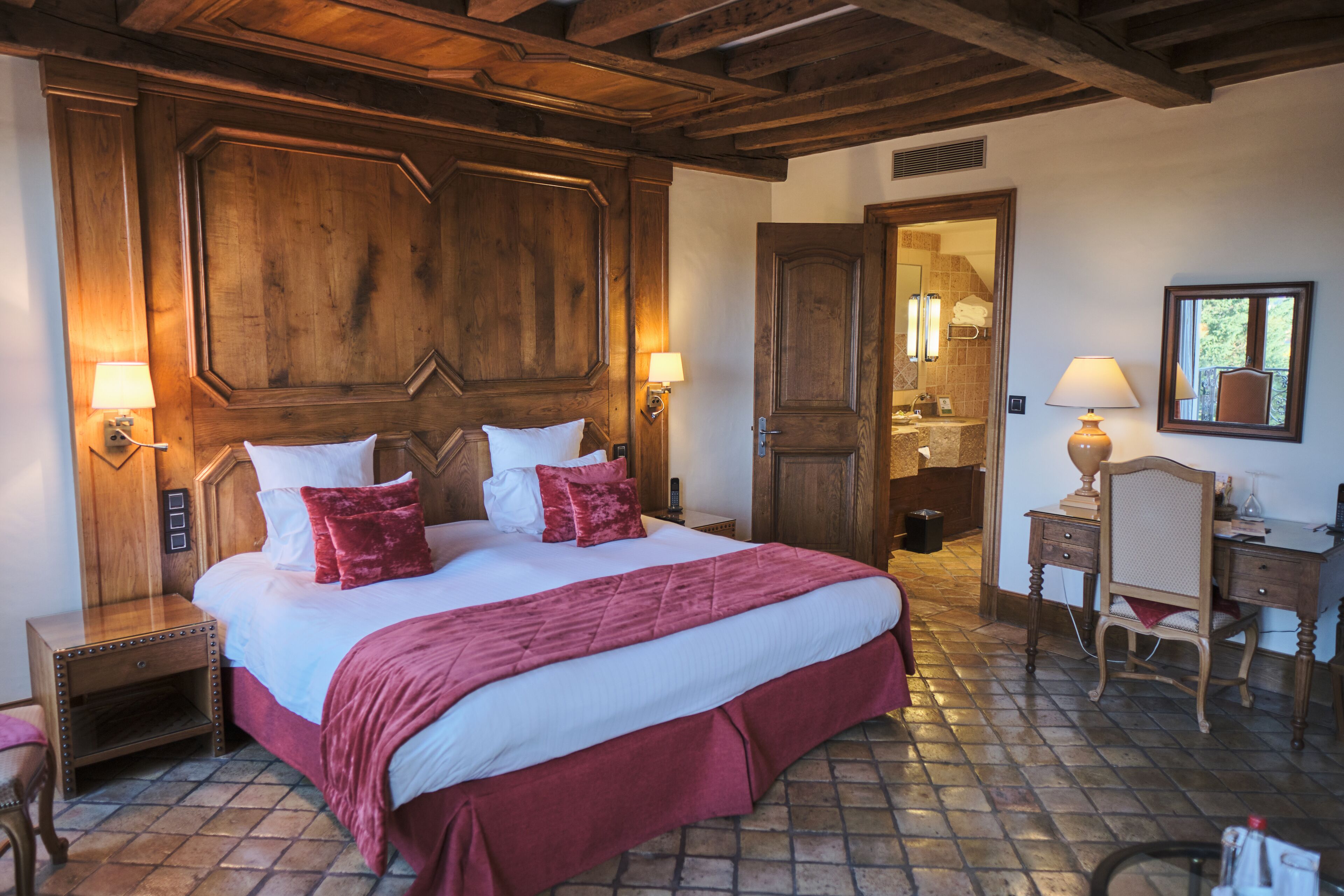 Ein Hotelzimmer mit einem großen Bett, einem Holzkopfstück, zwei Nachttischen mit Lampen, einem Holzbüro mit Stuhl und einem durchgehenden Türspalt sichtbaren Badezimmer.