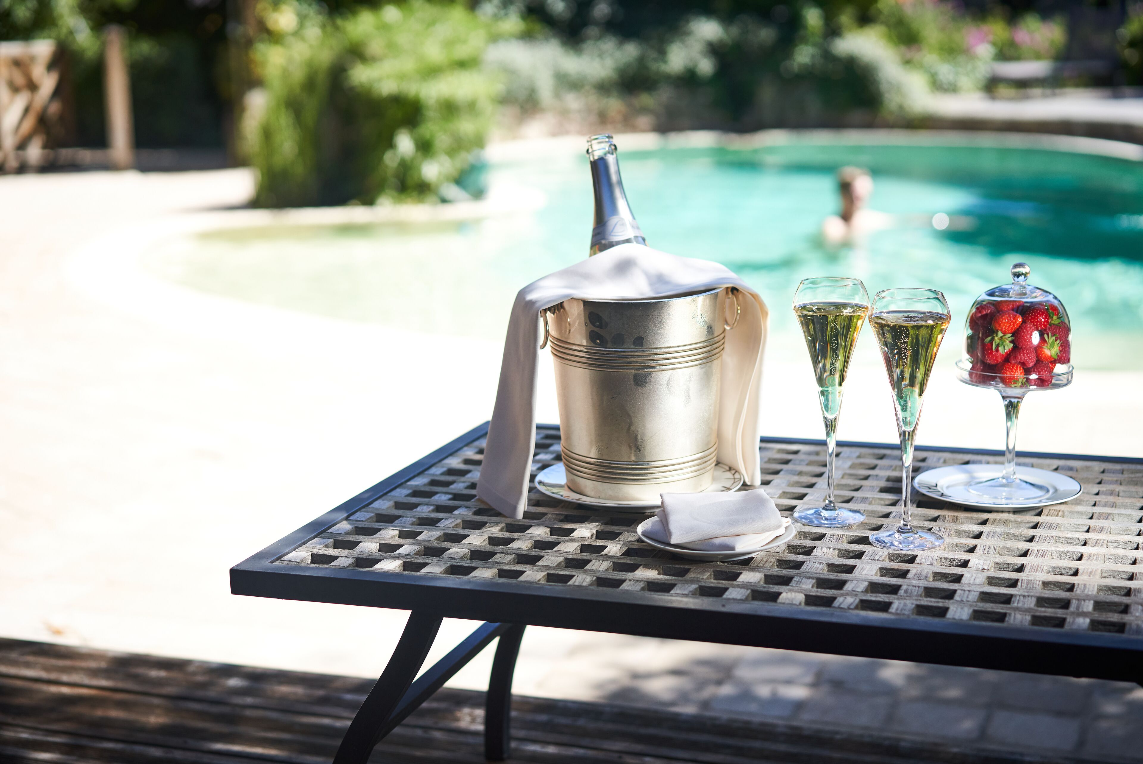 A table with a metal bucket, two glasses, and a glass dome with strawberries.